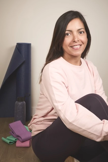 Yasmin Morales sentada con ropa deportiva rosa junto a una esterilla y material de ejercicio.